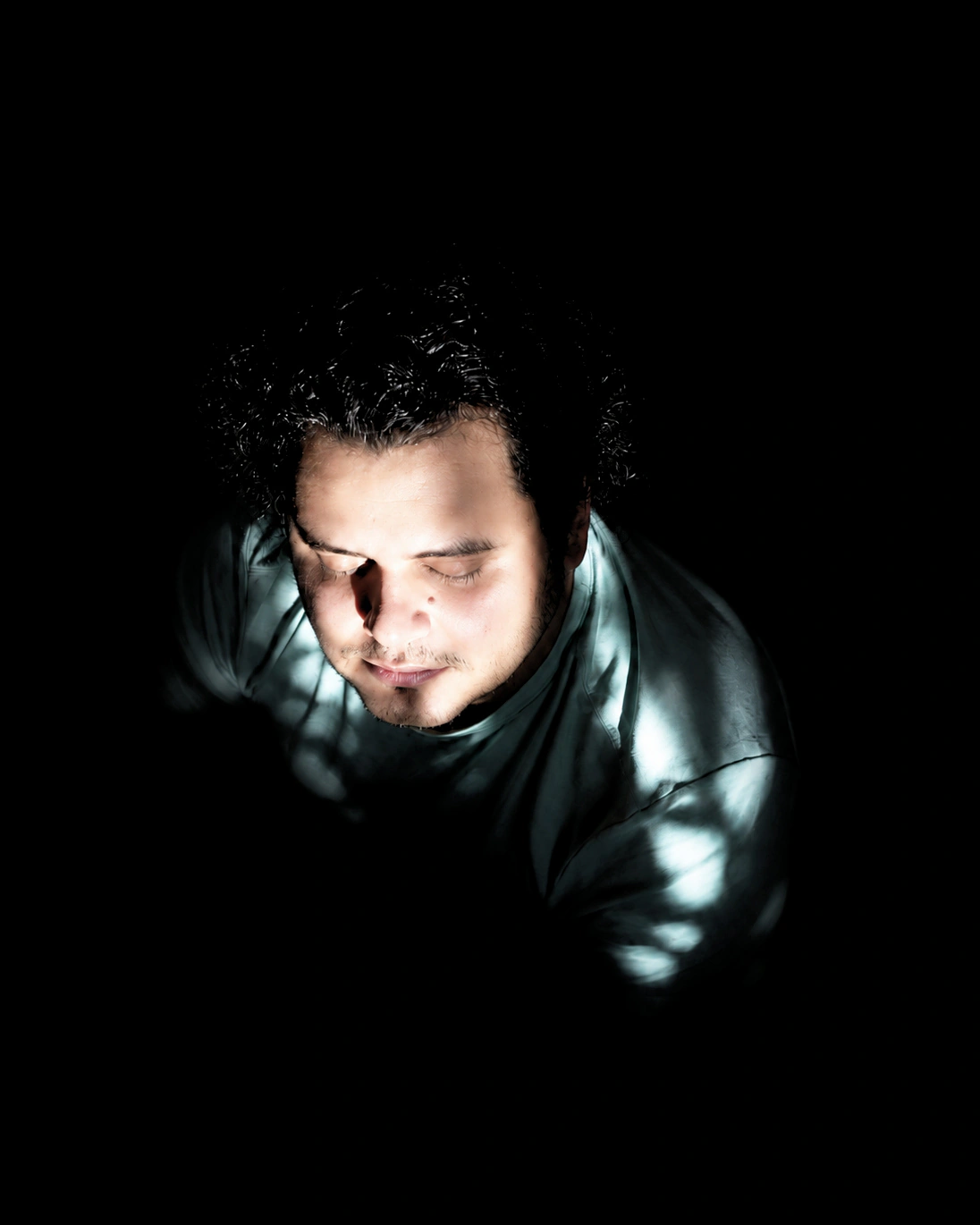 SeyedRasool Sadrieh, eyes closed, lit from above in a dark room